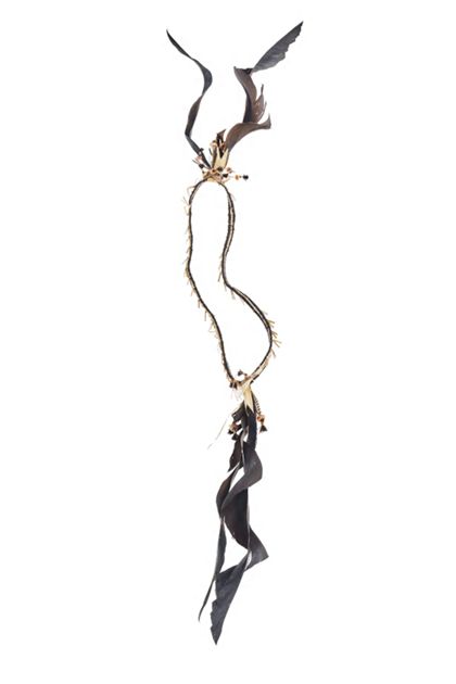 Kopfschmuck, dessen Reif aus Stroh und Menschenhaar geflochten ist. Seitlich sind Haifisch-Zähne, kleine Korallen-Scheibchen und je zwei schwarze Federn angehängt.