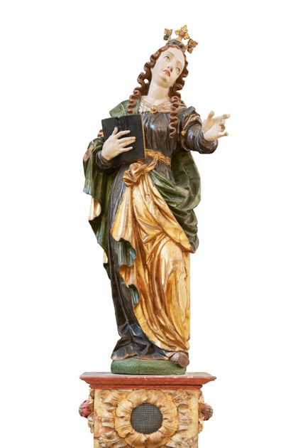 Auf einem Sockel stehende weibliche Heilige, die mit der Linken einen Zeigegestus ausführt und in der Rechten ein Buch hält.