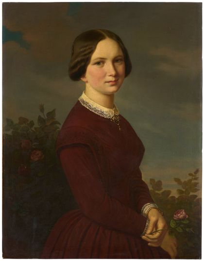 Ein junges Mädchen mit braunem Haar in einem roten Kleid steht vor einem Rosenbusch und hält eine Rose in der Hand.