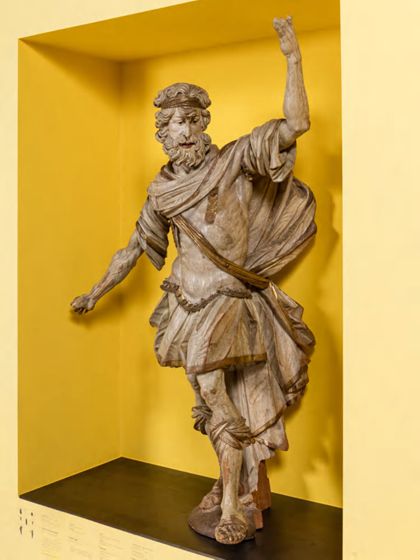 Überlebensgroße, monochrom hell gefasste Skulptur des Samson als Kanzelträger in römisch-antiker Soldatenbekleidung, seitliche Ansicht.