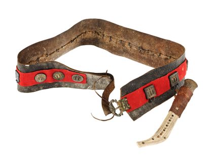 Ein breiter Ledergürtel mit mittig laufendem roten Filzband und darauf angebrachten runden und quadratischen Metallplaketten. Seitlich befestigt hängt ein Messer in heller Messerscheide.