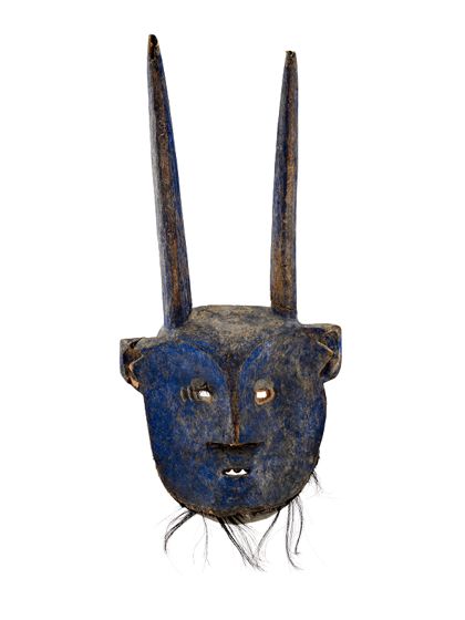 Maske aus Holz mit Hörnern. Ein Auge ist mit einer Glaseinlage versehen. Die Zähne bestehen aus pflanzlichem Material, die Barthaaare und eine Augenbraue sind mit Fellstücken eingeklebt. Am Rand befinden sich zahlreiche Bohrungen. Die Maske weist blaue Bemalung auf.